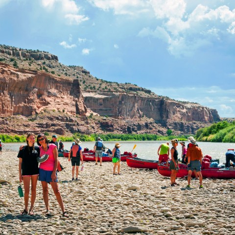 People with canoes on a rocky riverbank with cliffs in the background.