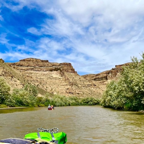 Canoeing on a river with rocky cliffs and trees under a blue sky.
