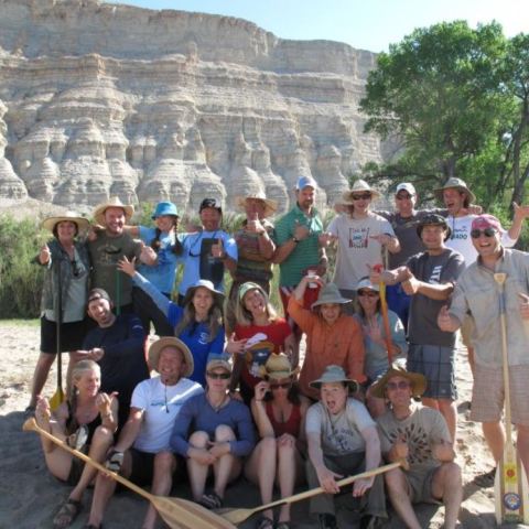 Group of people with paddles posing in front of rocky cliffs and tree.