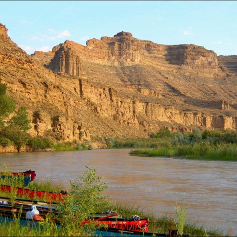 Colorful canoes by a river with rocky cliffs in the background under a clear sky.