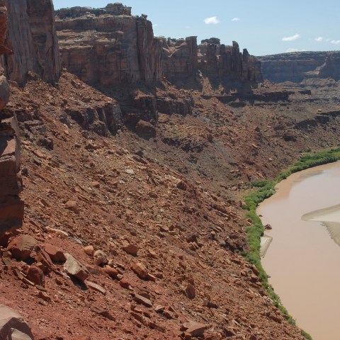 Person standing on a rocky cliff overlooking a winding river in a desert canyon.