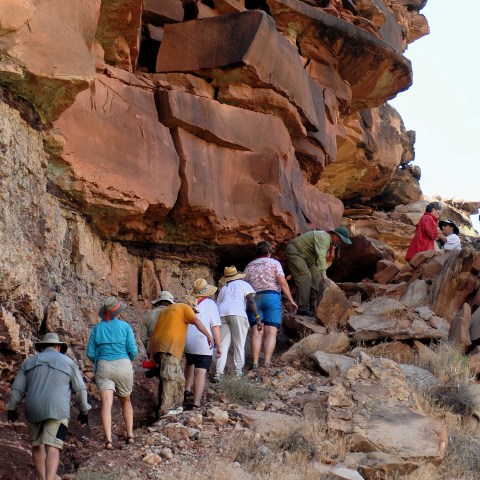 Group hiking along rocky cliffside trail under an overhang.