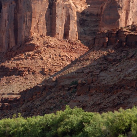 Canoes on a river with red rock cliffs and green bushes in the background.
