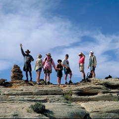 Group of hikers standing on rocky terrain with a stack of stones, under a blue sky.