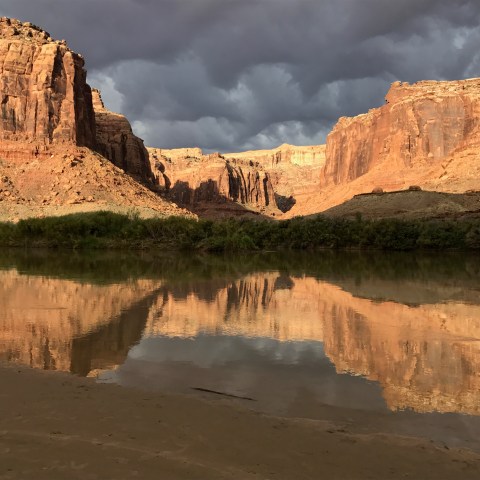 Canyon landscape with river reflecting rocky cliffs beneath a cloudy sky.