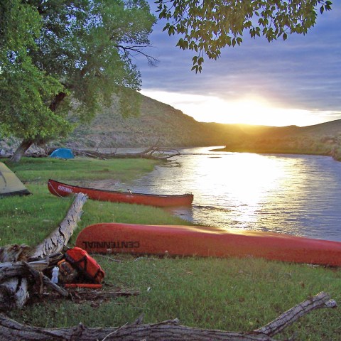 Riverside campsite with tents, canoes, and sunrise.