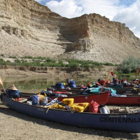 Canoes loaded with gear on a riverbank with cliffs and bushes in the background.
