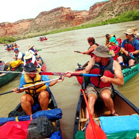 Group of people canoeing on a river with rocky cliffs in the background.