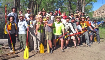 Group of people with paddles standing outdoors in a wooded area.