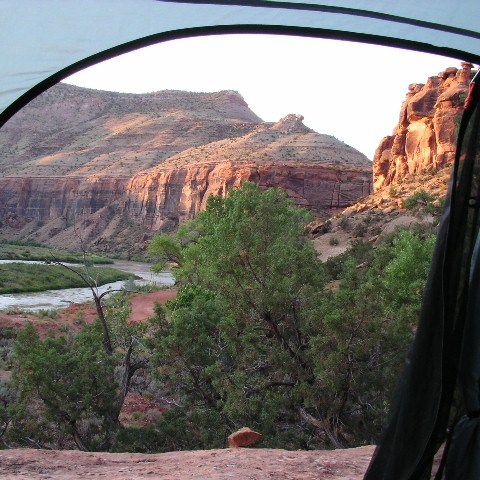 View of rocky canyon landscape through open tent doorway, with river and trees.