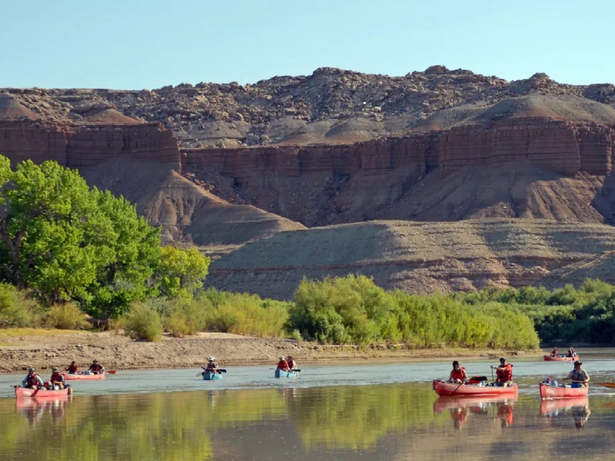People kayaking on a calm river with rocky hills and greenery in the background.